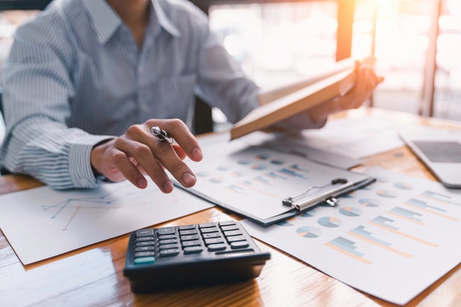 Cette image représente une personne calculant son retour sur investissement à l'aide de graphiques et d'une calculatrice