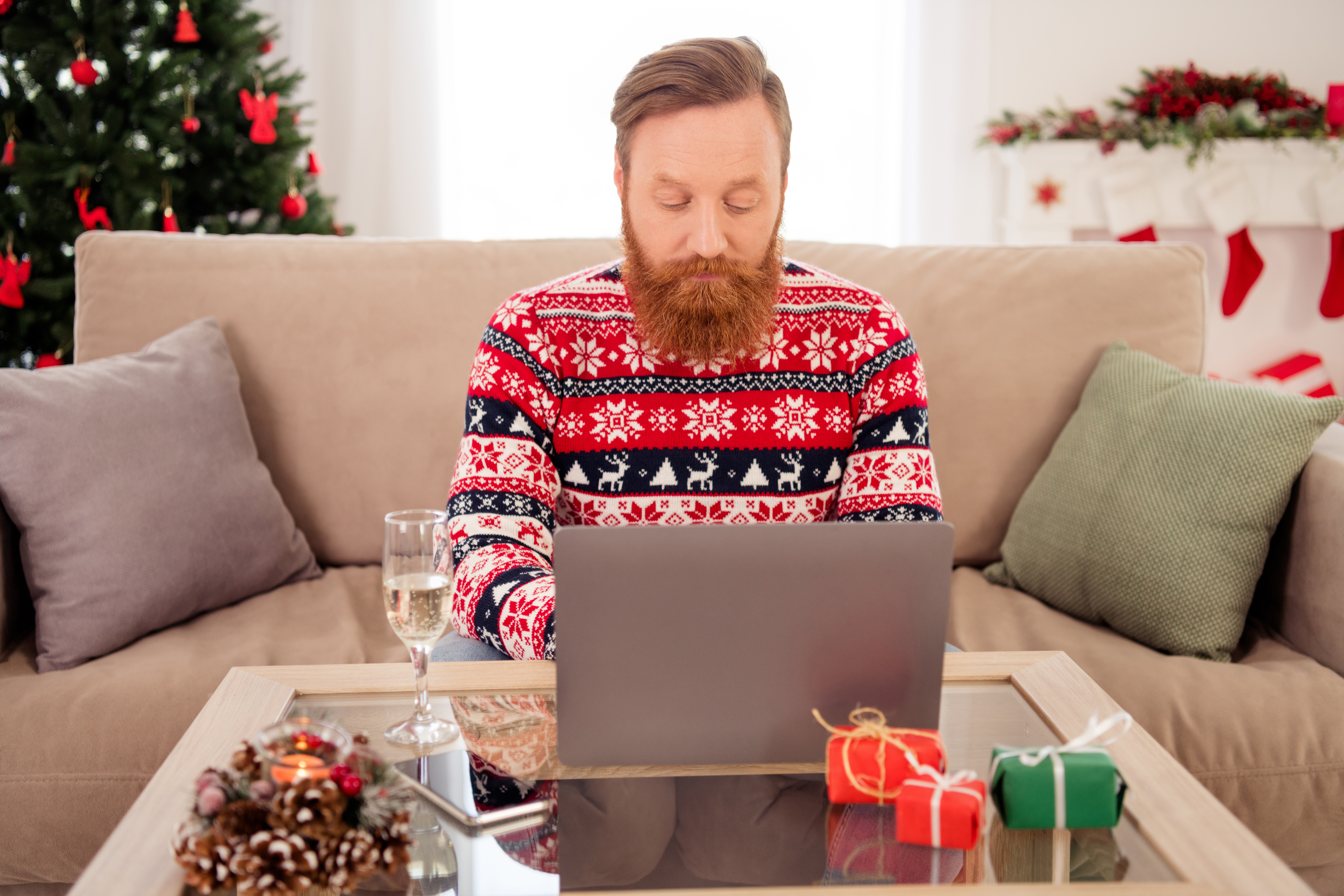 un homme avec un pull de Noel qui travaille sur son ordinateur portable